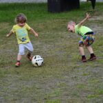 Dwóch małych chłopców kopiących piłkę.