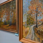 Trzy obrazy w ramkach wiszą na ścianie w rzędzie obok siebie. Prace przedstawiają krajobrazy jesienne, czyli drzewa pokryte złotymi liśćmi i aleje prowadzące wzdłuż nich.