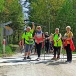 Cztery kobiety stoją na środku drogi. Wspierają sie na kijkach do nordic walkingu. Uśmiechają się. Jest słoneczna pogoda