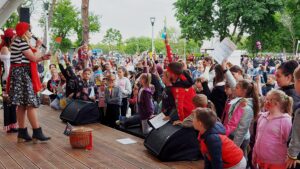 Tłum dzieci przed sceną. Wyciągają wgóre ręcejakby zgłaszały się do odpowiedzi.Na sceniedwie osoby w strojach piratów.