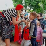 Kobieta przebrana w stój piratki nachyla się nad małym chłopcem. Trzyma w ręce mikrofon, do którego chłopiec coś mówi. W tle grupa innych dzieci.