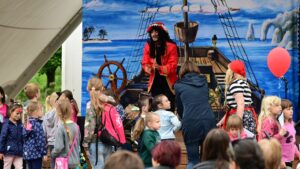 Na scenie mężczyzna przebrany za pirata. Scenografia przedstawia statek piracki na morzy. Przed sceną dzieci ogldające spektakl.