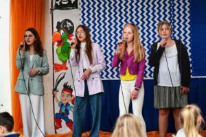 Cztery nastoletnie dziewczyki stoją na scenie. śpiewają do mikrofonów.
