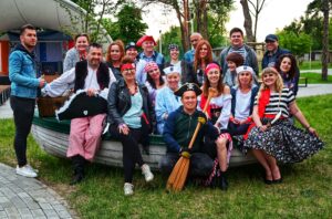 Kilkanaście osób siedzi w łodzi rybackiej. Ubrani są w stroje żeglarzy i piratów.
