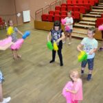 Dzieci tańczące na sali widowiskowej. W rękach trzymają kolorowe pompony do tańca.