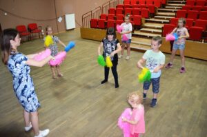 Dzieci tańczące na sali widowiskowej. W rękach trzymają kolorowe pompony do tańca.
