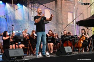 Scena. W tle orkiestra symfoniczna. Na froncie woklaista trzymający mikrofon.