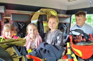 Czworo dzieci siedzi w kabinie samochodu strażackiego.