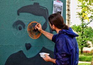 Młody mężczyzna ubrany w kombinezon ochronny z kapturem. Maluje mural.