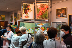 Grupa osób ogląda wystawę malarstwa. Obrazy to głównie martwa natura nawiązująca kolorystycvznie i tematycznie do jesieni.
