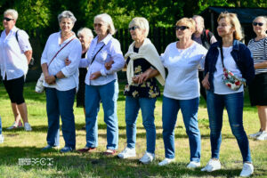 Kilka kobiet w wieku senioralnym. Są podobnie ubrane - w jeansy i białe koszule. Trzymają się pod ręce.