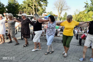 Kilka kobiet w wieku senioralnym. Obejmują się ramionami i tańczą.