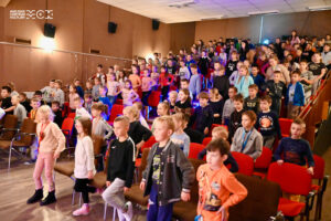 Dzieci w wieku szkolnym stojące na widowni sali widowiskowej.
