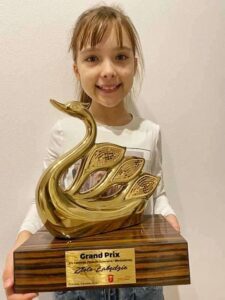 Dziewczynka trzymająca przed sobą dużą statuetkę nagrody Grand Prix w postaci złotego łabędzia. 