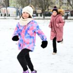 Trzy małe dziewczynki biegają po śniegu na dworze. Szeroko uśmiechają się.