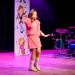 Młoda dziewczynka śpiewa na scenie do publiczności.