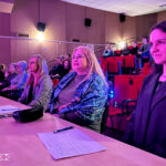 Trzy dorosłe kobiety siedzą przy stoliku przed sceną. Prawdopodobnie pełnią funkcję jury.