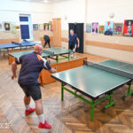 Zdjęcie przedstawia rozgrywki tenisa stołowego wśród dorosłych mężczyzn.