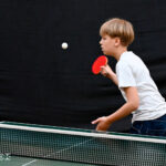 Zdjęcie przedstawia chłopca grającego na stole do tenisa. Na jego twarzach widać skupienie.