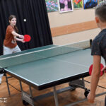 Zdjęcie przedstawia dzieci grające na stołach do tenisa. Na ich twarzach widać skupienie.