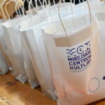 Zdjęcie przedstawia nagrody rzeczowe w papierowych torbach z logo Miejskiego Centrum Kultury.