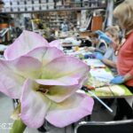 Zdjęcie przedstawia grupę kobiet pracującą podczas warsztatów tworzenia kwiatu z foamiranu. Na pierwszym planie widoczny jest wykonany kwiat.